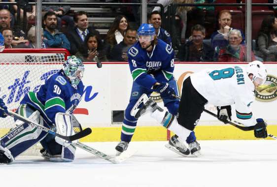 VANCOUVER, BC - FEBRUARY 28: Christopher Tanev #8 of the Vancouver Canucks checks Joe Pavelski #8 of the San Jose Sharks as Ryan Miller #30 of the Canucks eyes the puck during their NHL game at Rogers Arena February 28, 2016 in Vancouver, British Columbia, Canada. (Photo by Jeff Vinnick/NHLI via Getty Images)
