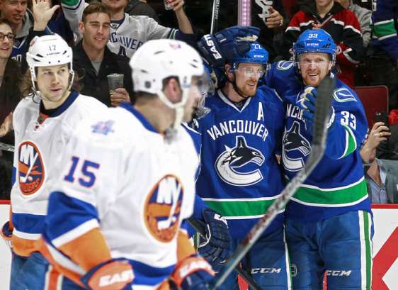 VANCOUVER, BC - MARCH 1: Henrik Sedin #33 congratulates goal scorer Daniel Sedin #22 of the Vancouver Canucks in front of Cal Clutterbuck #15 and Matt Martin #17 of the New York Islanders during their NHL game at Rogers Arena March 1, 2016 in Vancouver, British Columbia, Canada. New York won 3-2. (Photo by Jeff Vinnick/NHLI via Getty Images)